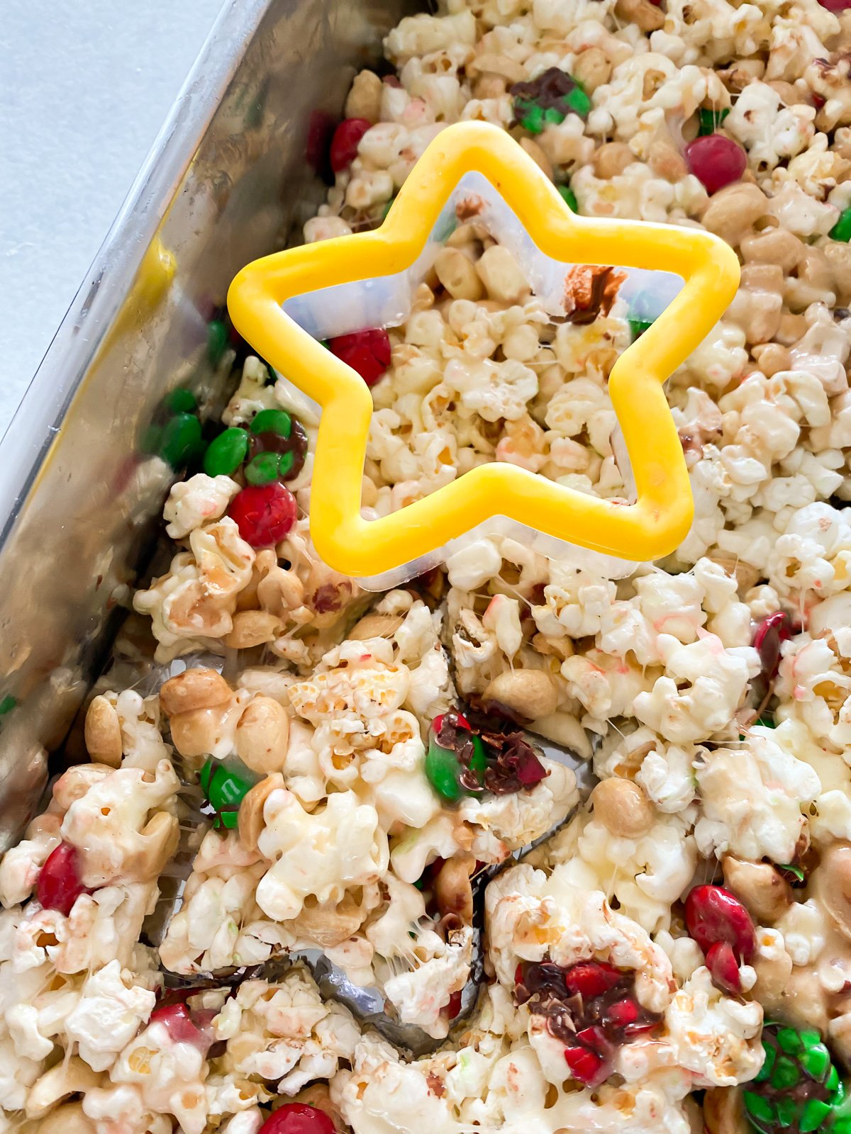 menggunakan pemotong kue bintang untuk memotong bentuknya menjadi selembar camilan popcorn marshmallow.
