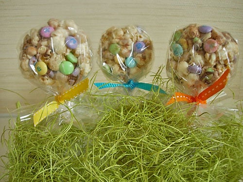 Resep dan petunjuk Popcorn-Cake-Lollipop Resep Kue Popcorn dibuat menjadi bentuk lollipop dengan tusukan lidi ke dalamnya. Pita diikatkan pada batang dan diletakkan di atas rumput Paskah.